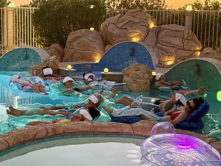 Guests floating on pool loungers with eye towels during the Naughty and Nice floating sound bath at Blisstopia Retreats in Peoria Arizona